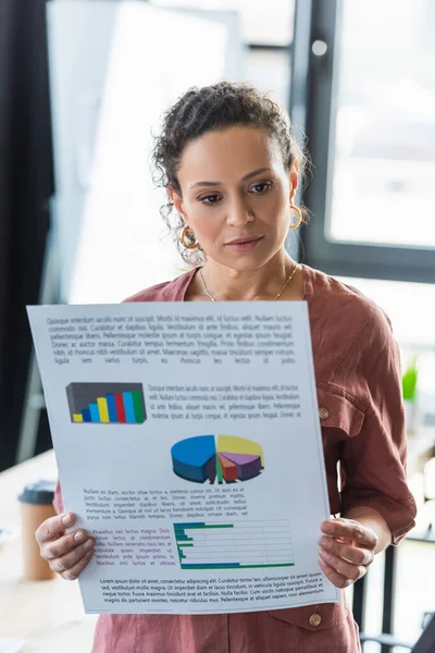 Африканская американская бизнесвумен держит бумагу с графиками в офисе — стоковое фото