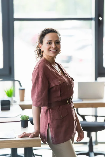 African american businesswoman in casual clothes smiling at camera near working table — Stock Photo