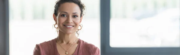 Positiva mujer de negocios afroamericana mirando la cámara en la oficina, pancarta - foto de stock