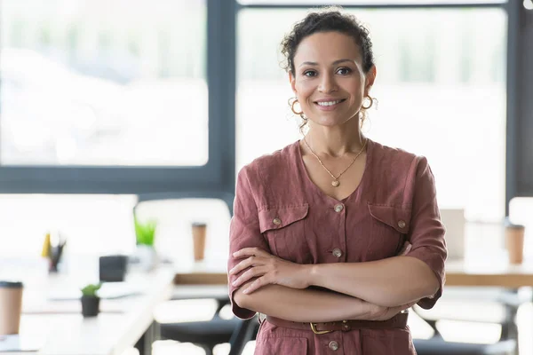 Positive african american businesswoman crossing arms in office — Stock Photo