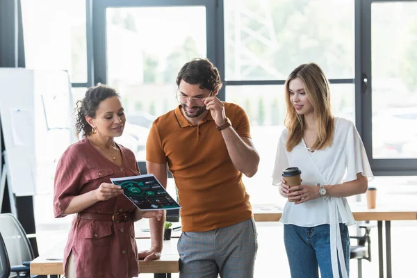 Smiling african american businesswoman holding paper near colleagues with coffee in office — Stock Photo