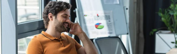 Empresário sorrindo falando no telefone celular perto gráfico flip borrado no escritório, banner — Fotografia de Stock
