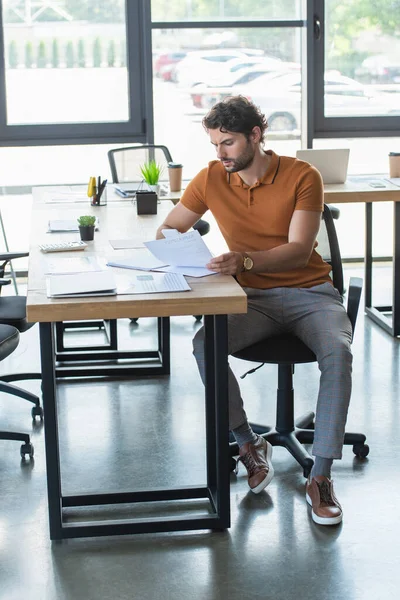 Geschäftsmann schaut sich Dokumente auf Arbeitstisch im Büro an — Stockfoto