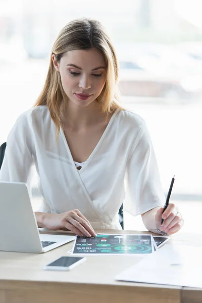 Joven empresaria sosteniendo pluma cerca de papeles y gadgets en la oficina - foto de stock