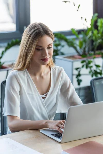 Pretty businesswoman using laptop near paper folder in office — Stock Photo