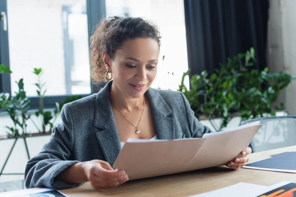 Souriante femme d'affaires afro-américaine regardant le dossier papier dans le bureau — Photo de stock