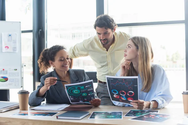 Smiling african american businesswoman pointing at document near colleagues and paper folder in office — Stock Photo