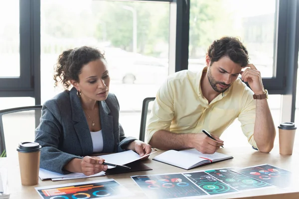 Interracial business people working with charts on papers near coffee to go in office — Stock Photo