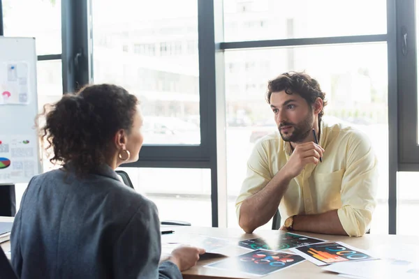 Businessman holding pen and talking to african american colleague near documents in office — Stock Photo