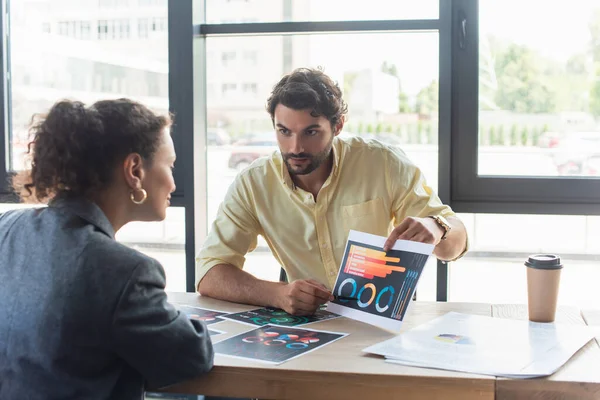 Businessman pointing at charts on document near african american colleague in office — Stock Photo