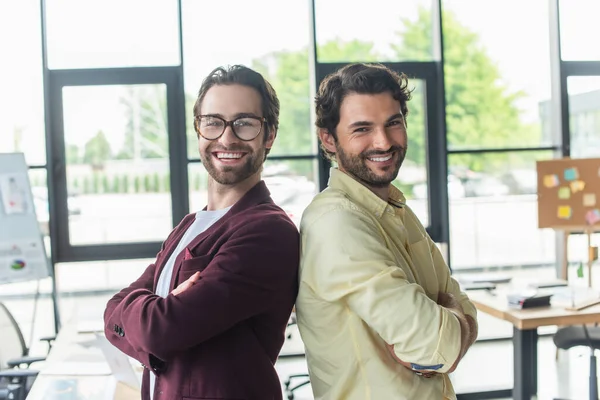 Felices hombres de negocios con los brazos cruzados de pie espalda con espalda en el cargo - foto de stock