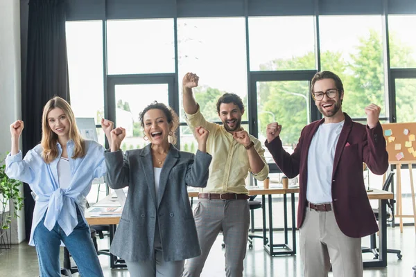 Aufgeregte multiethnische Geschäftsleute zeigen Ja-Geste und blicken in die Kamera im Büro — Stockfoto