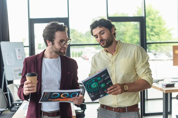 Empresário segurando papel e conversando com colega sorridente com café para ir no escritório — Fotografia de Stock