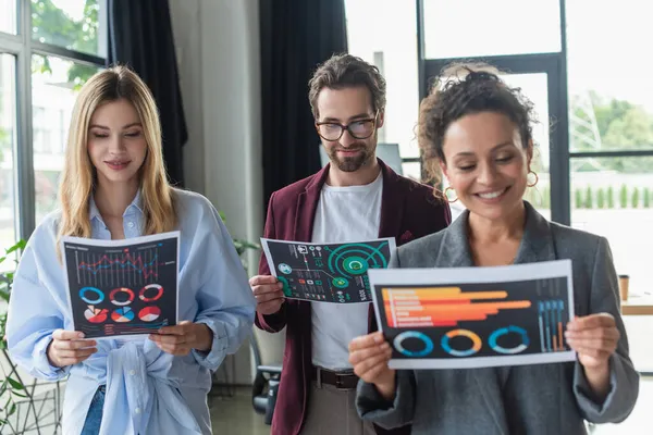 Businessman in eyeglasses looking at paper near multiethnic colleagues in office — Stock Photo