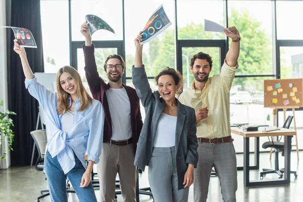 Heureux hommes d'affaires multiethniques soulevant des documents au bureau — Photo de stock