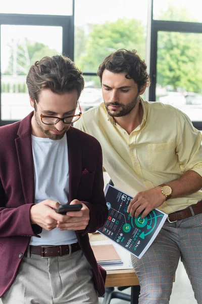 Businessman using cellphone near colleague with document in office — Stock Photo