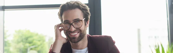 Young businessman in eyeglasses smiling at camera in office, banner — Stock Photo