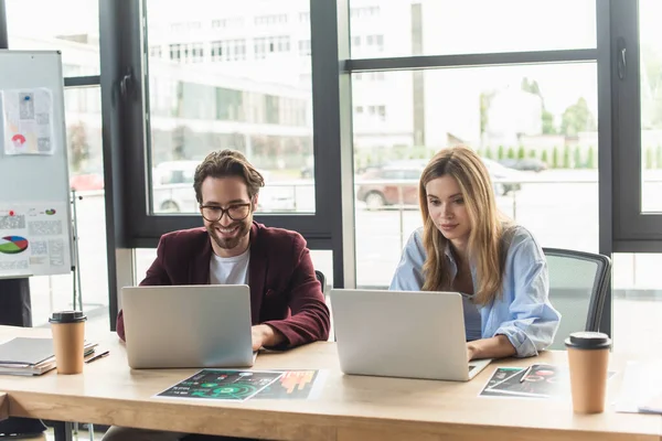 Jóvenes empresarios que usan computadoras portátiles cerca del café para ir y documentos en la oficina — Stock Photo