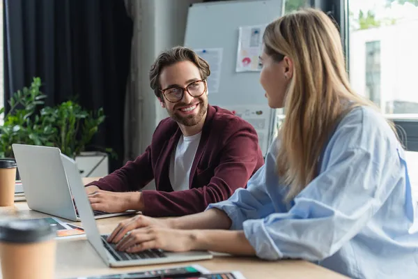 Smiling businessman looking at blurred colleague using laptop in office — Stock Photo