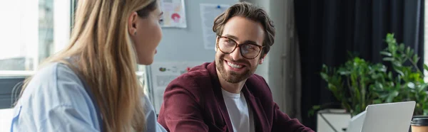 Junger Geschäftsmann schaut verschwommenen Kollegen in der Nähe von Laptops im Büro an, Banner — Stockfoto