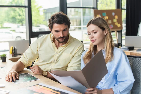 Young businesswoman holding paper folder near colleague in office — Stock Photo