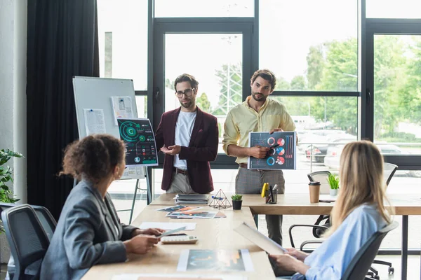 Businessmen holding documents near interracial colleagues in office — Stock Photo