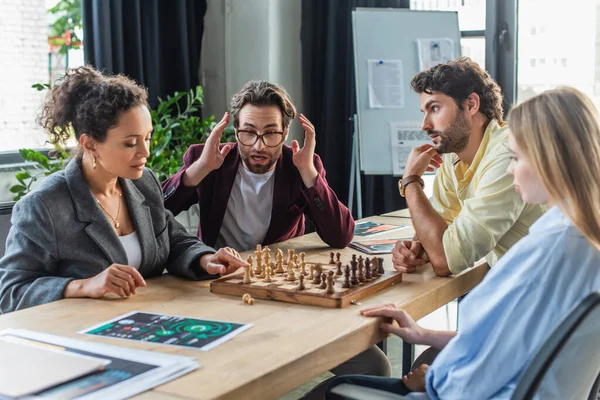 Schockierter Geschäftsmann sitzt neben multiethnischen Kollegen und spielt Schach im Büro — Stockfoto