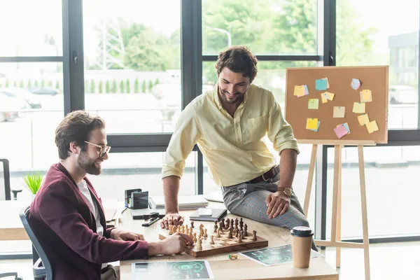 Hombres de negocios sonrientes jugando ajedrez cerca del café para ir a la oficina - foto de stock