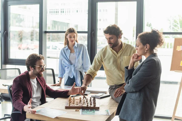 Businessmen playing chess near interracial colleagues and papers in office — Stock Photo