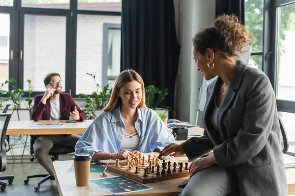 Interrassische Geschäftsfrauen spielen Schach neben verschwommener Kollegin im Büro — Stockfoto