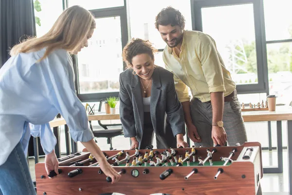 Les gens d'affaires interraciaux positifs s'amusent tout en jouant au baby-foot au bureau — Photo de stock