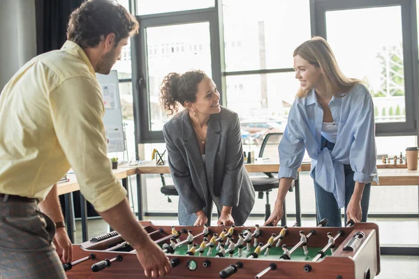 Lächelnde Geschäftsleute beim Tischkicker mit afrikanisch-amerikanischen Kollegen im Büro — Stockfoto