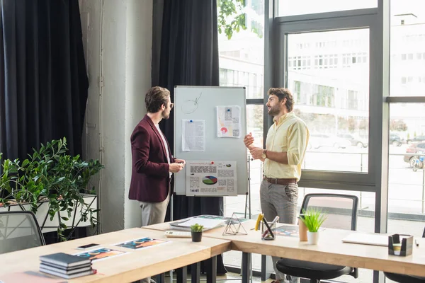 Geschäftsmann spricht mit Kollege in der Nähe von Flipchart im Büro — Stockfoto