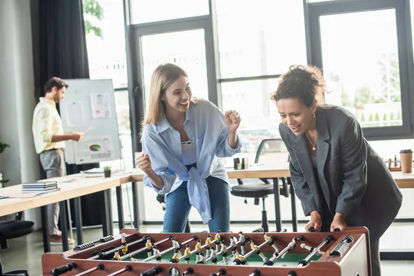 Empresária entusiasmada mostrando sim gesto perto de colega afro-americano jogando futebol de mesa no escritório — Fotografia de Stock