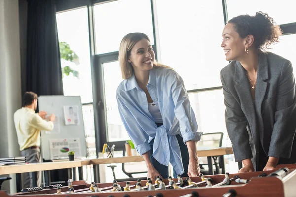 Mulheres de negócios inter-raciais olhando umas para as outras enquanto jogam futebol de mesa no escritório — Fotografia de Stock