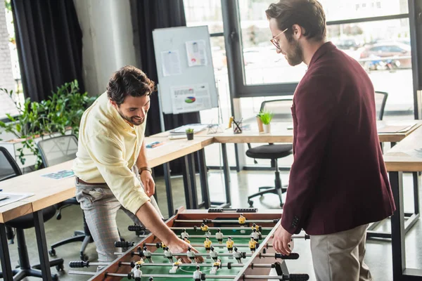 Positive businessman in formal wear playing table football in office — Stock Photo