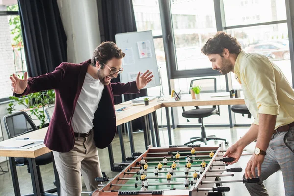 Empresário animado jogando futebol de mesa com colega no escritório — Fotografia de Stock