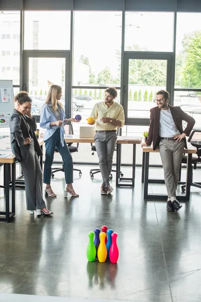 Lächelnde Geschäftsleute mit Bällen in der Nähe von Bowling im Büro — Stockfoto