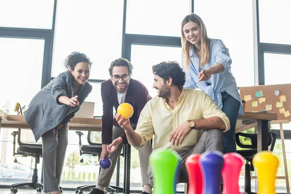 Geschäftsmann hält Bowlingball neben lächelnden Kollegen im Büro — Stockfoto