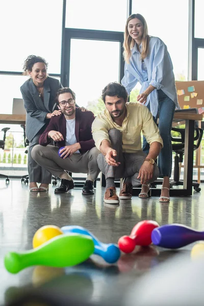 Homme d'affaires jouant au bowling près de souriants collègues interracial au bureau — Photo de stock