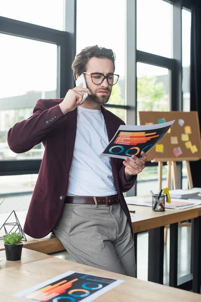 Geschäftsmann mit Brille spricht auf Smartphone und hält Dokument im Büro — Stockfoto