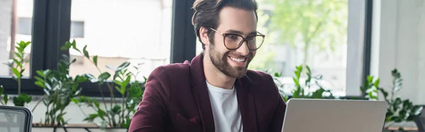 Homme d'affaires heureux dans les lunettes regardant ordinateur portable dans le bureau, bannière — Photo de stock