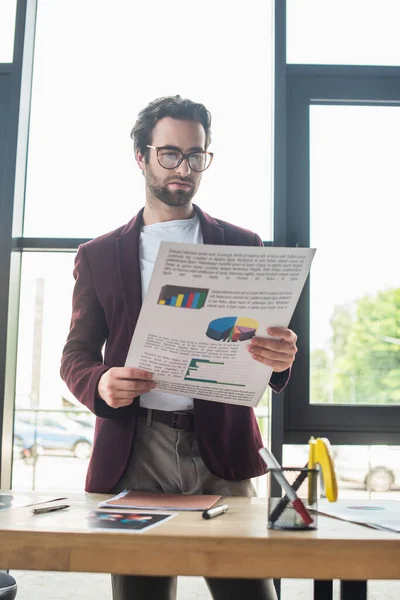 Jeune homme d'affaires tenant un document près de la table de travail au bureau — Photo de stock