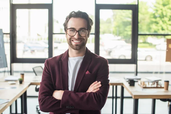 Junger lächelnder Geschäftsmann mit Brille blickt in verschwommenem Büro in die Kamera — Stockfoto