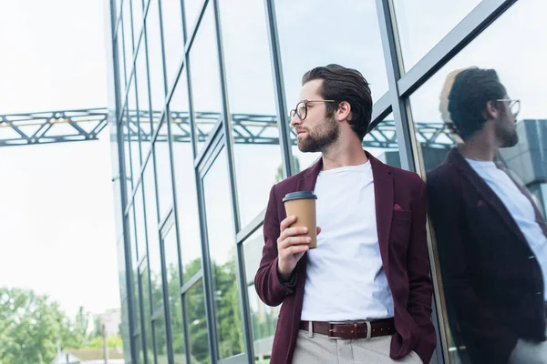 Side view of young businessman holding takeaway drink near building outdoors — Stock Photo