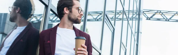 Side view of businessman in eyeglasses holding coffee to go near building on urban street, banner — Stock Photo