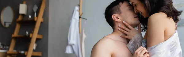 Vue latérale de la jeune femme souriant tout en embrassant avec un homme passionné dans la chambre à coucher, bannière — Photo de stock