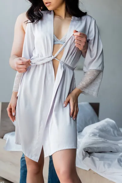 Cropped view of shirtless man untying silk robe on brunette woman — Stock Photo