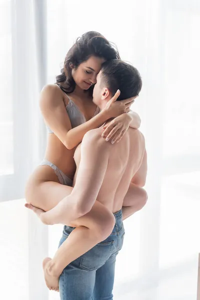 Без рубашки мужчина в джинсах поднимает соблазнительную женщину в сексуальном белье — стоковое фото