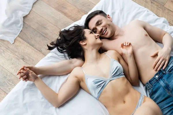 Vue de dessus de l'homme torse nu et femme heureuse en lingerie couchée sur le lit — Photo de stock